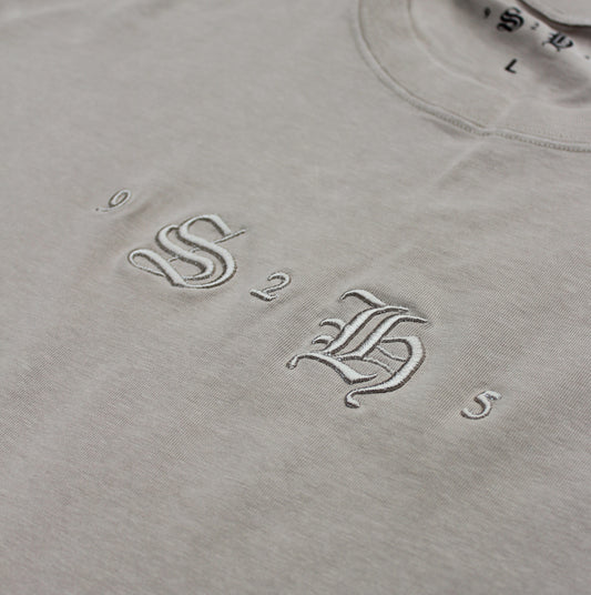 Close-up of the Classic Embroidered T-Shirt by silverhollowjewellery, made from 100% cotton in beige with vintage-style white "9 S B 2 5" embroidery and a visible "L" size label.