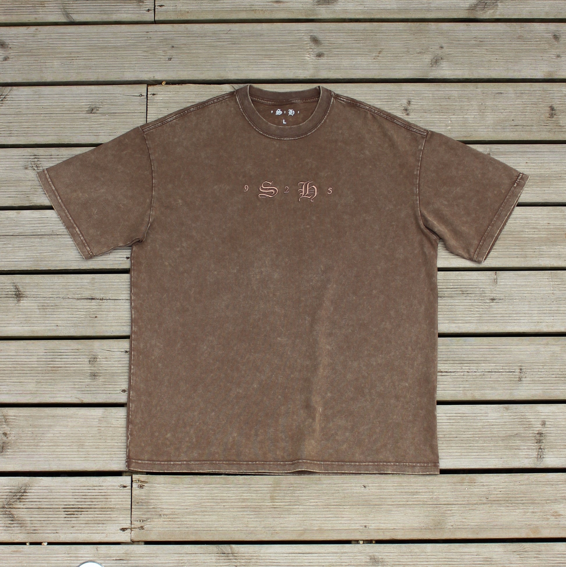 The Classic Embroidered T-Shirt by silverhollowjewellery, a brown 100% cotton short-sleeved tee featuring "S H" on the chest, is displayed flat on wooden planks.