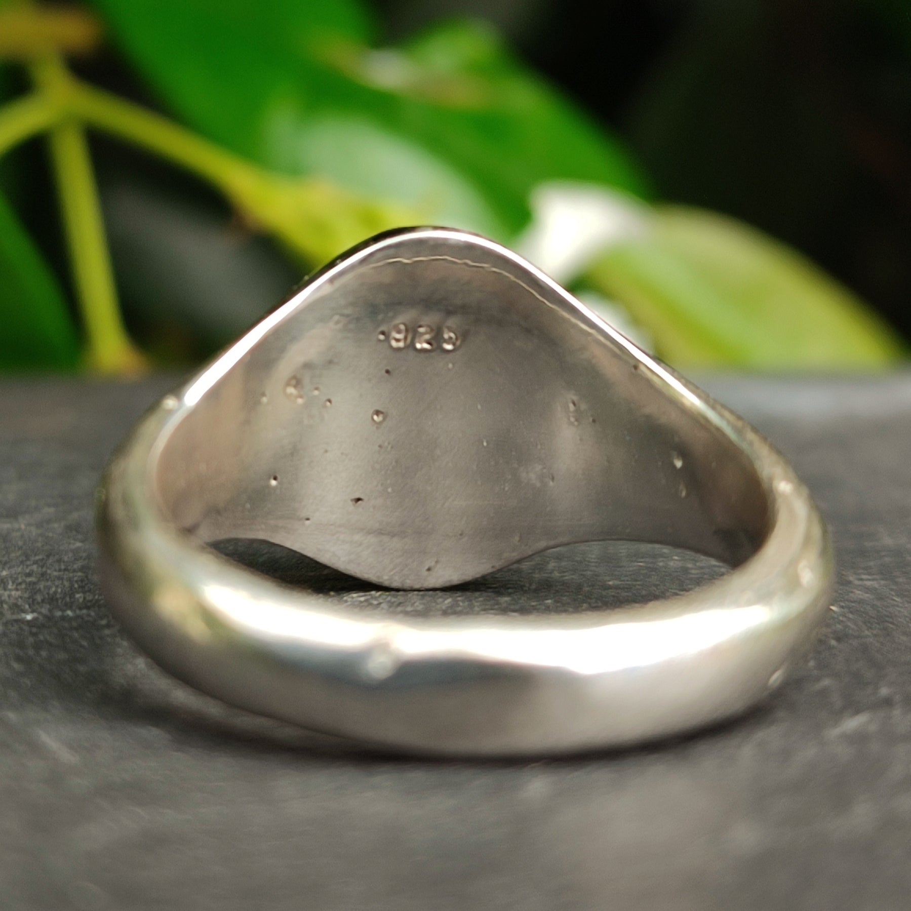 A close-up shows the inner band of the silverhollowjewellery Citrine Sterling Silver Ring, featuring a "925" hallmark for authenticity, set against softly blurred green leaves.