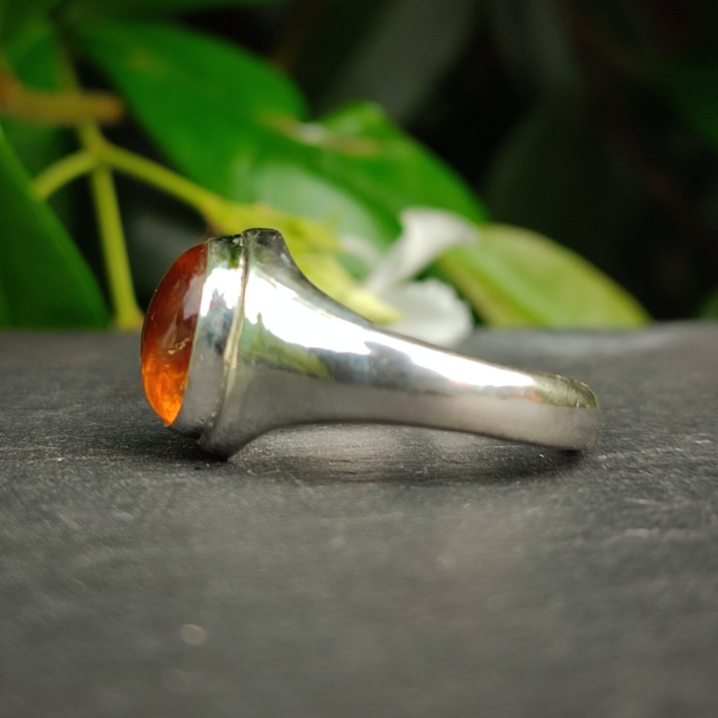 The Citrine Sterling Silver Ring by silverhollowjewellery is pictured on a dark surface with green leaves behind it—a striking piece of handcrafted jewelry.