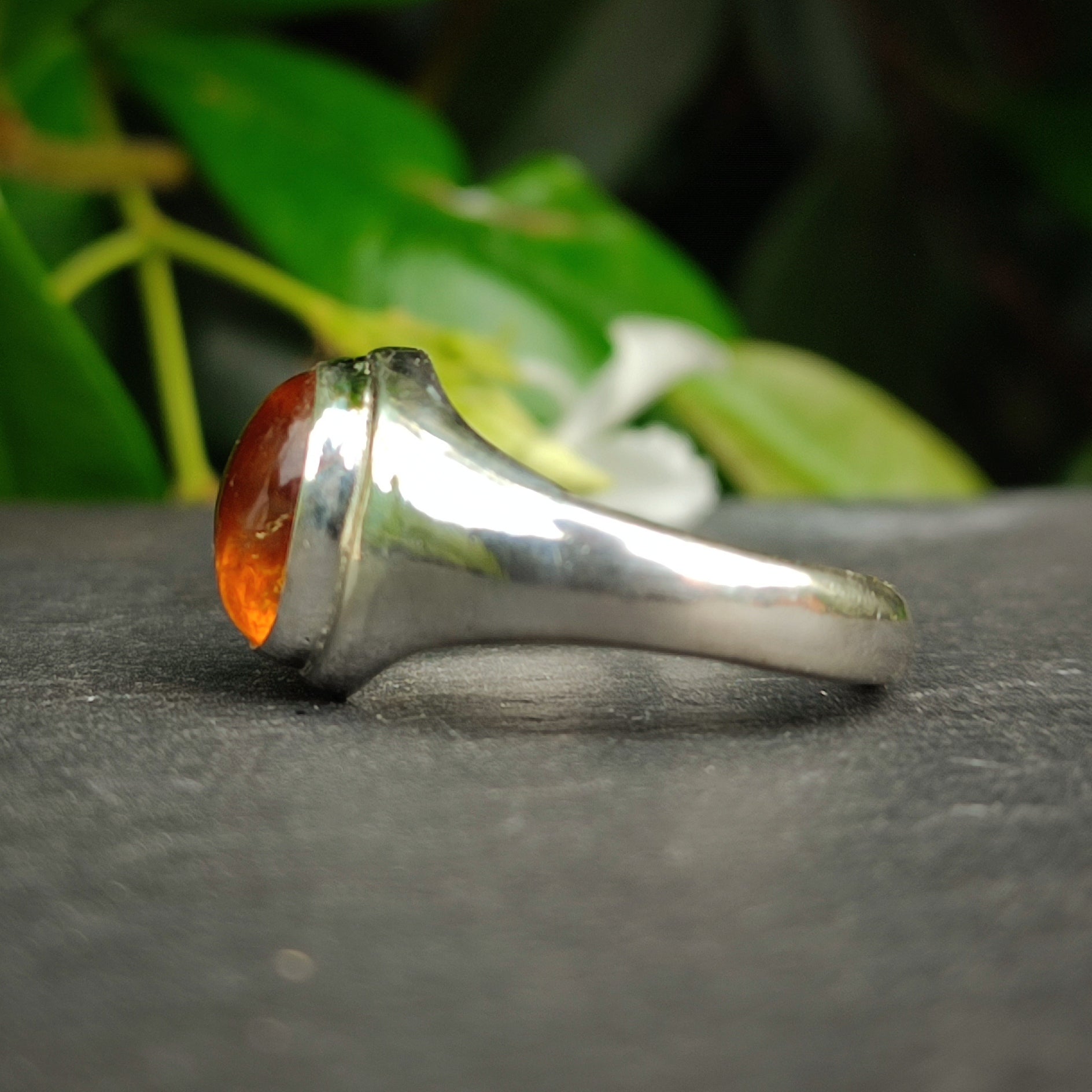 The Citrine Sterling Silver Ring by silverhollowjewellery is pictured on a dark surface with green leaves behind it—a striking piece of handcrafted jewelry.