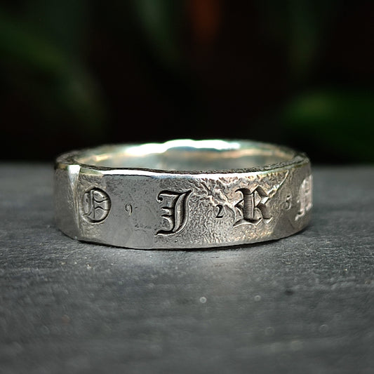The Custom Distressed Hallmark Ring by silverhollowjewellery features engraved gothic "O J R" letters on textured recycled sterling silver, displayed against a dark background.