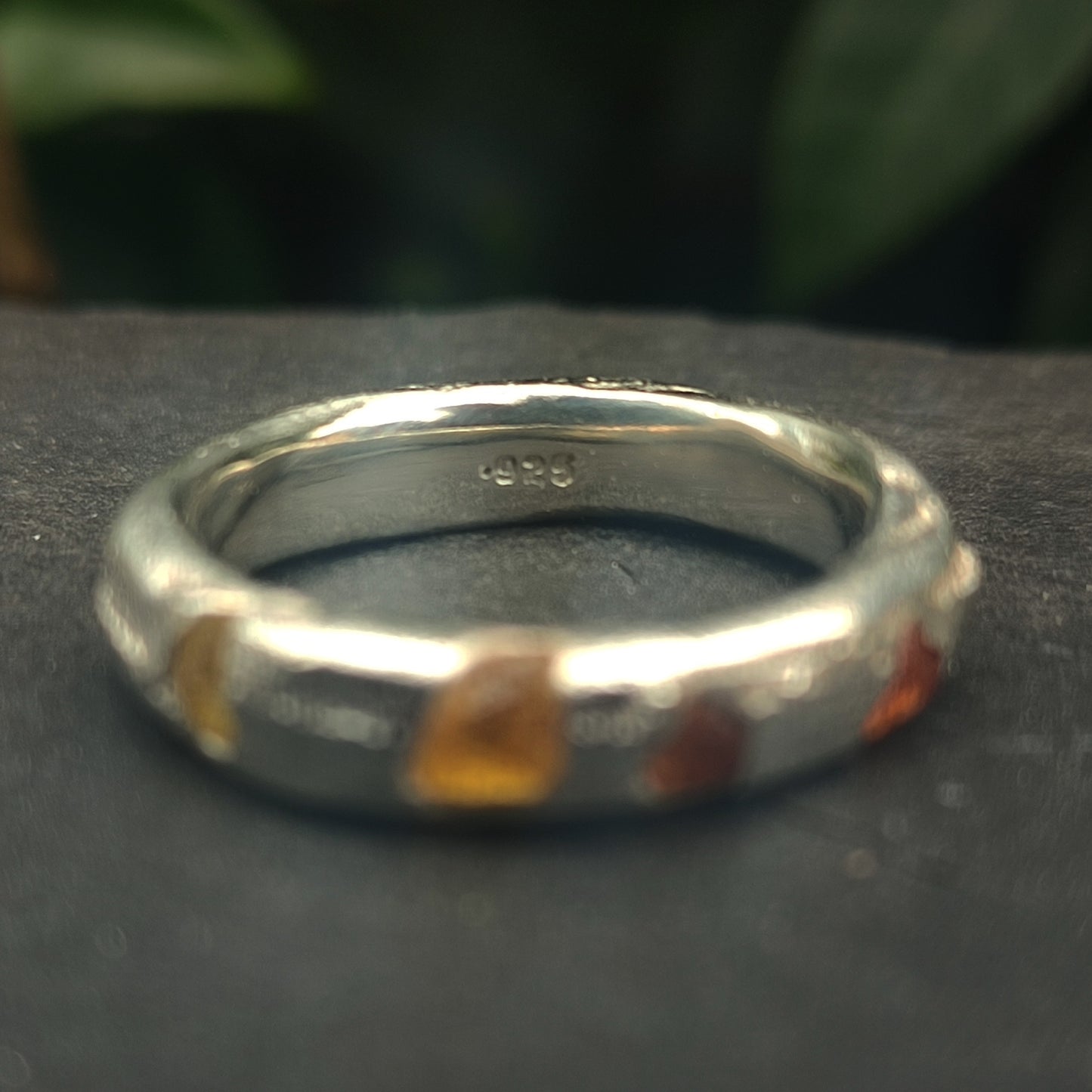 The Raw Sapphire Band Sterling Silver-Custom by silverhollowjewellery is an organic 925-stamped recycled silver ring with small raw sapphires set around the band, shown resting on a dark surface with greenery in the background.