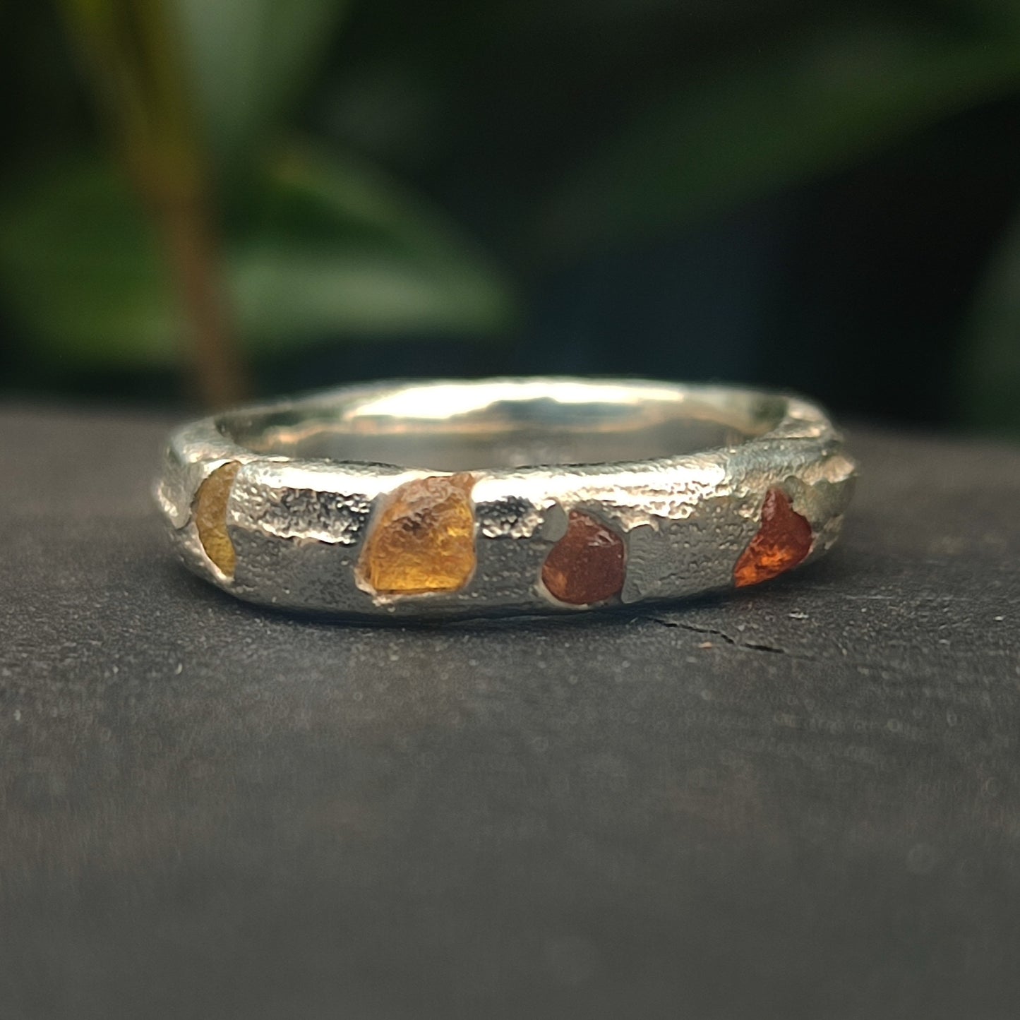 The Raw Sapphire Band Sterling Silver- Custom by silverhollowjewellery is a handcrafted sterling silver ring with a textured finish and raw sapphire stones, shown on a dark surface against a blurred green background.