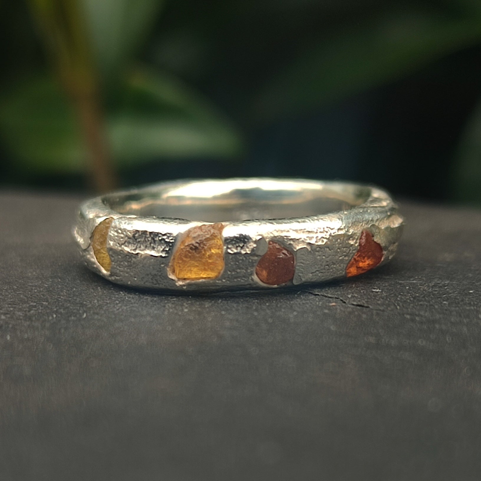 The Raw Sapphire Band Sterling Silver- Custom by silverhollowjewellery is a handcrafted sterling silver ring with a textured finish and raw sapphire stones, shown on a dark surface against a blurred green background.