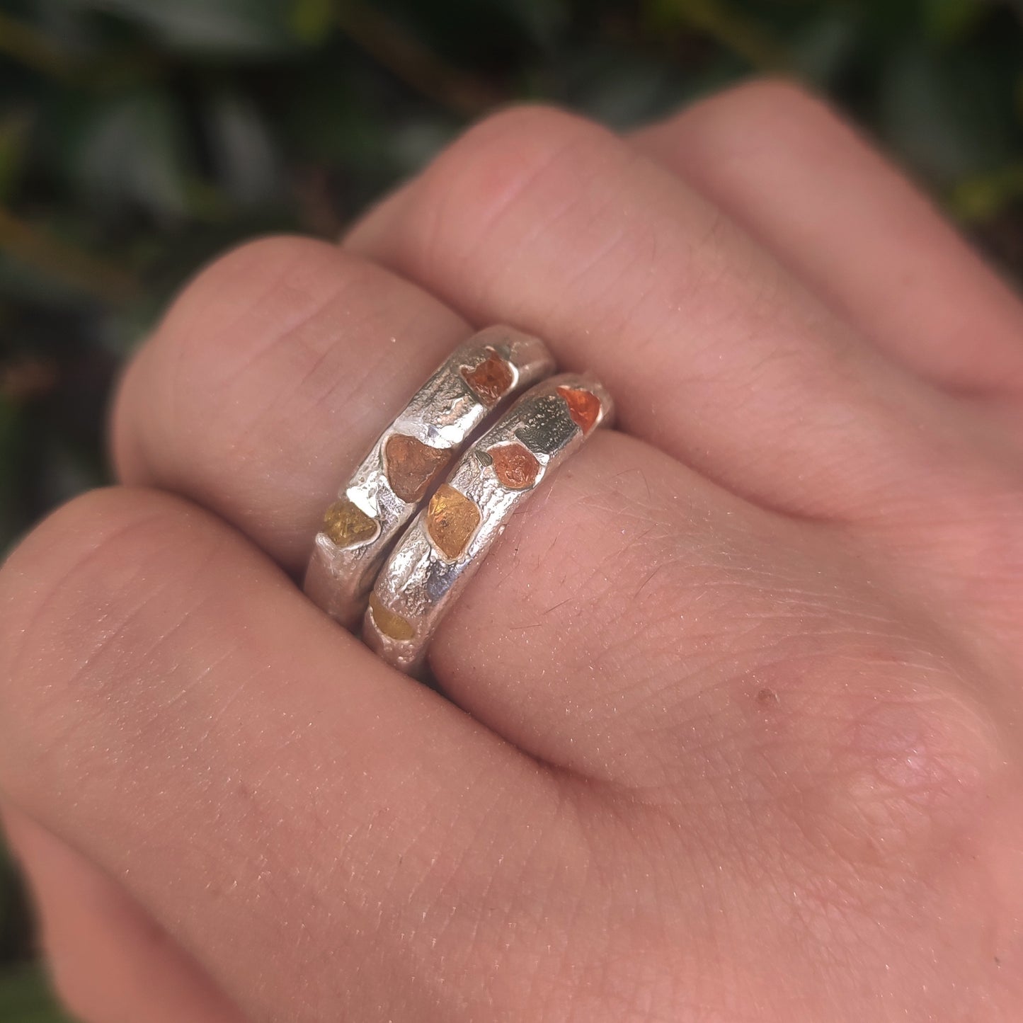 A hand wearing two silverhollowjewellery Raw Sapphire Band Sterling Silver-Custom rings, each adorned with small heart-shaped accents in different metallic hues.