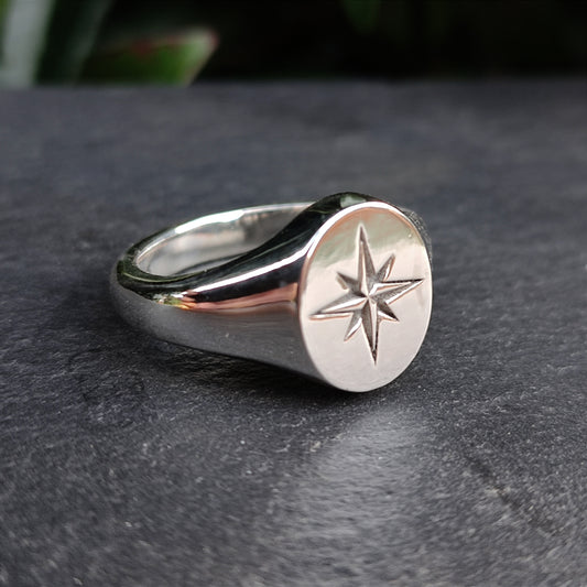 The North Star Signet Ring by silverhollowjewellery is crafted from recycled silver and features an engraved eight-pointed north star, shown on a dark stone surface.