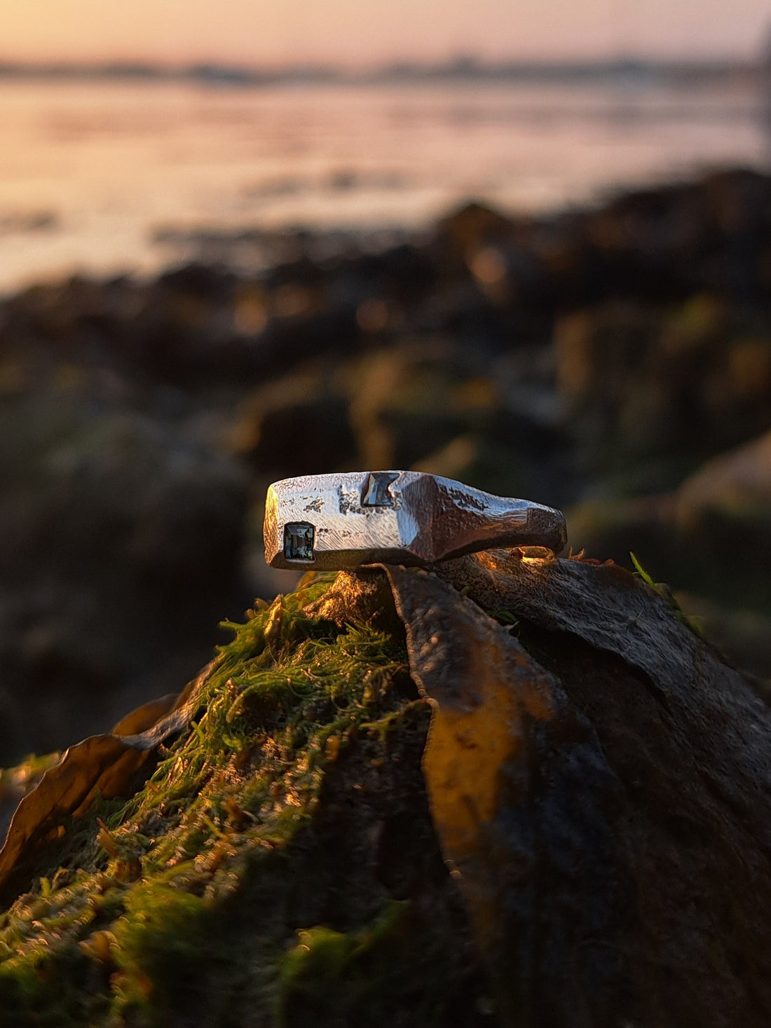 Sandcast silver sapphire ring made using sustainably sourced materials sat on a rock in nature by the sea