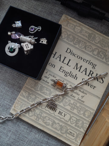 Range of silver charms on top of a leaflet about hall marks on english silver