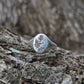 Silver ring with thistle engraving on a textured wooden surface