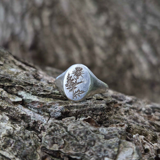 Silver ring with thistle engraving on a textured wooden surface