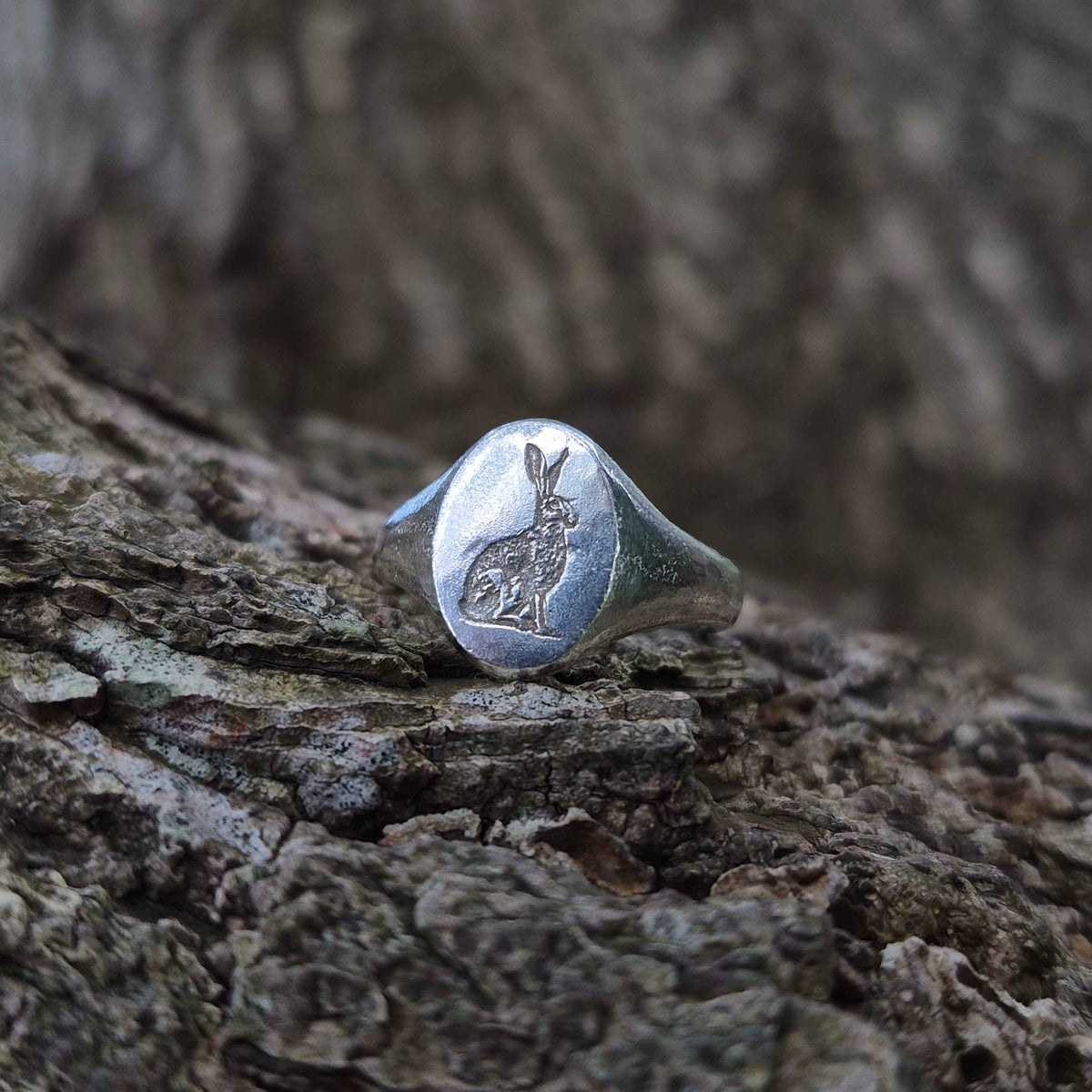 Silver signet ring with a engraved hare design on a wooden surface