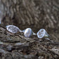 Three silver rings with engraved nature designs on a tree trunk.