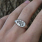 Silver ring with leaf design on a hand against a natural background