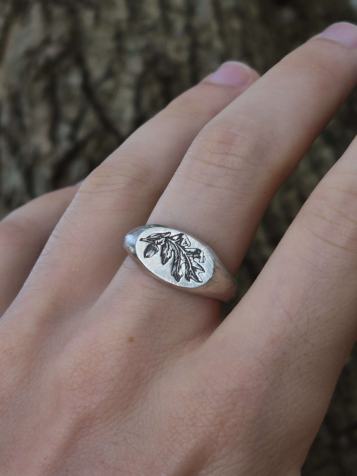Silver ring with leaf design on a hand against a natural background