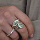 Close-up of a hand wearing two silver rings with leaf designs on a neutral background