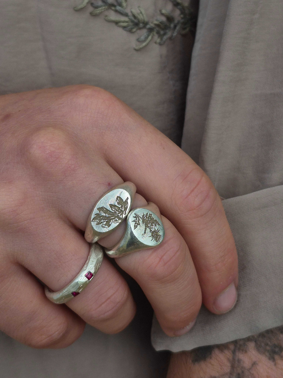Close-up of a hand wearing two silver rings with leaf designs on a neutral background