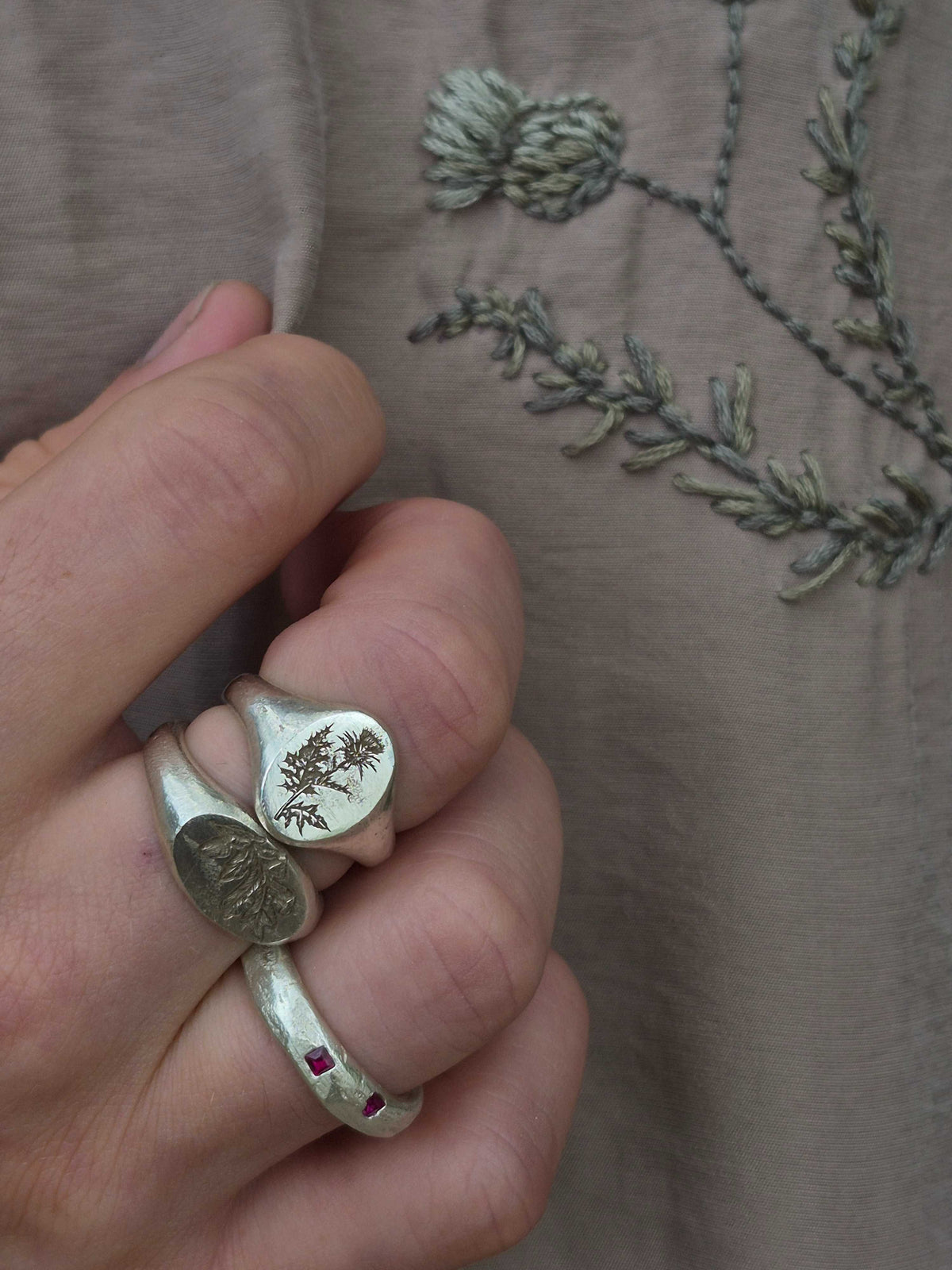 Silver ring with thistle design worn on a finger against a textured fabric background