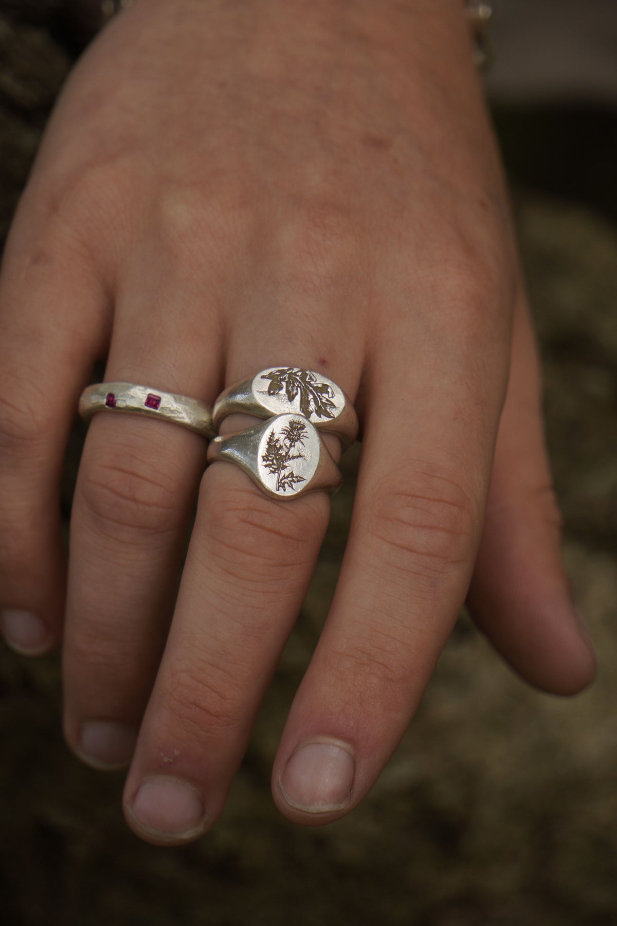Close-up of a hand wearing two silver rings with floral designs on a blurred background