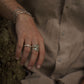 Close-up of a hand wearing three rings with a blurred person in a shirt in the background