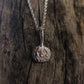The Pumpkin Pendant–Sterling Silver by silverhollowjewellery, a handcrafted necklace featuring a jack-o’-lantern design, rests on a textured wooden surface.