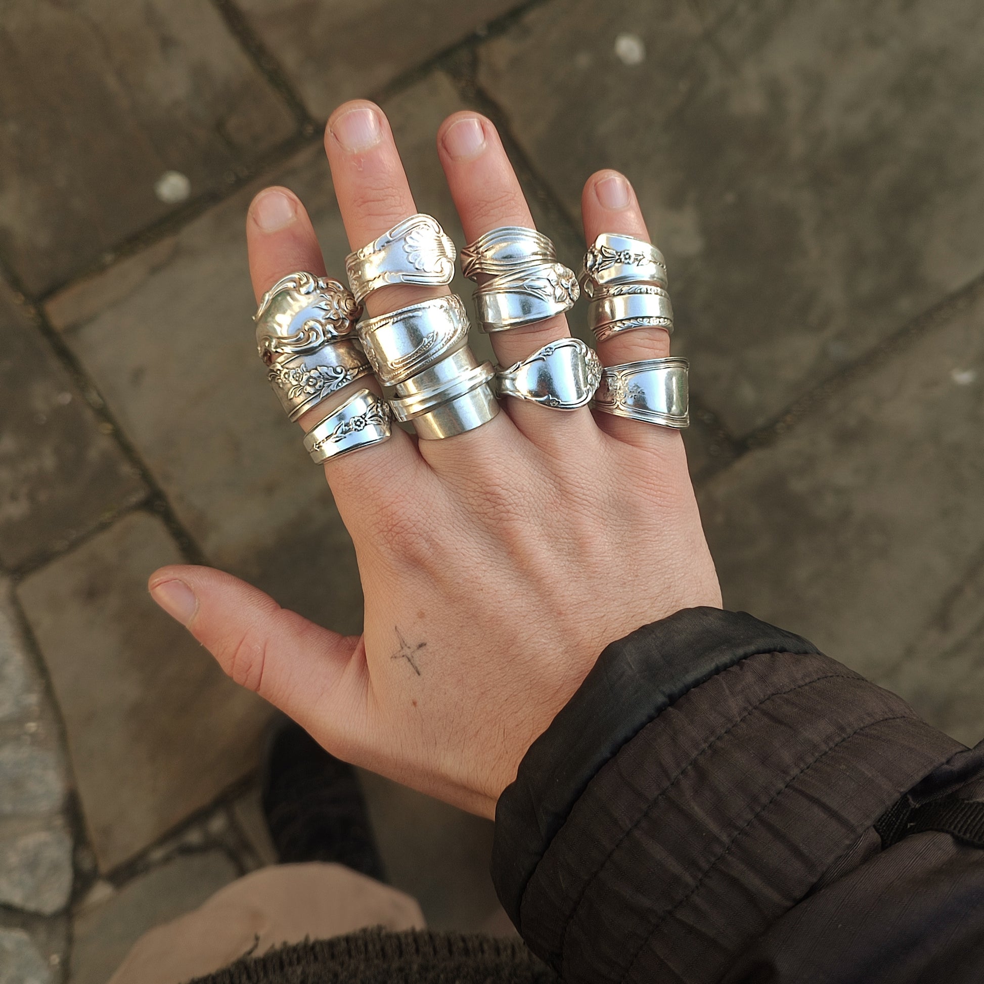 Hand wearing multiple silver rings on a stone pavement background