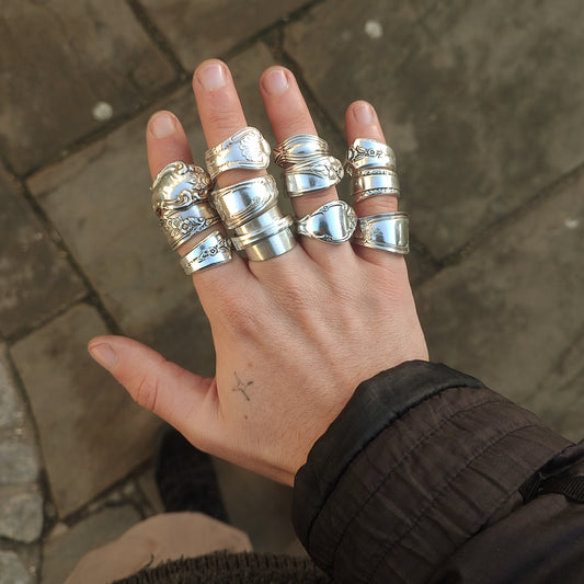 Hand wearing multiple silver rings on a stone pavement background