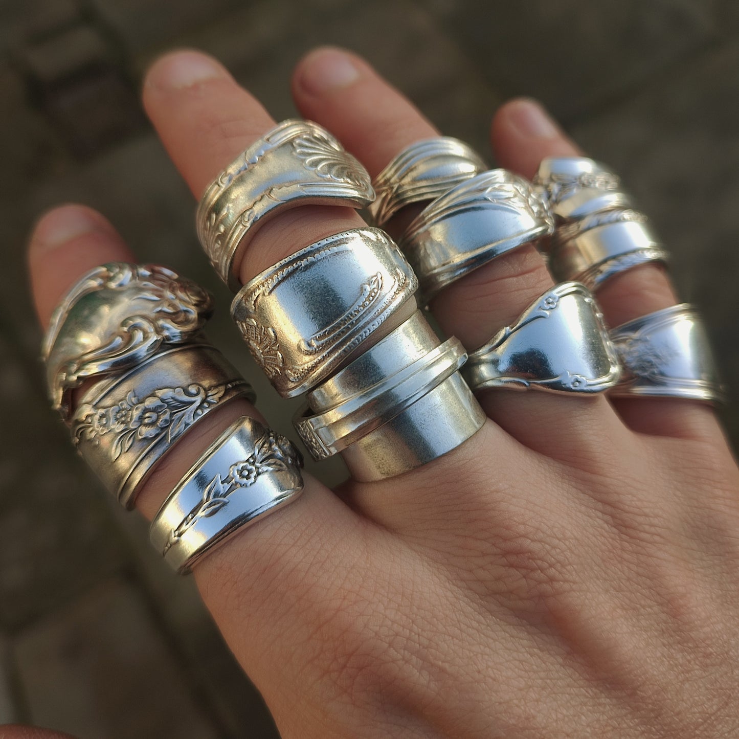 Hand wearing multiple spoon rings with intricate designs on a blurred background