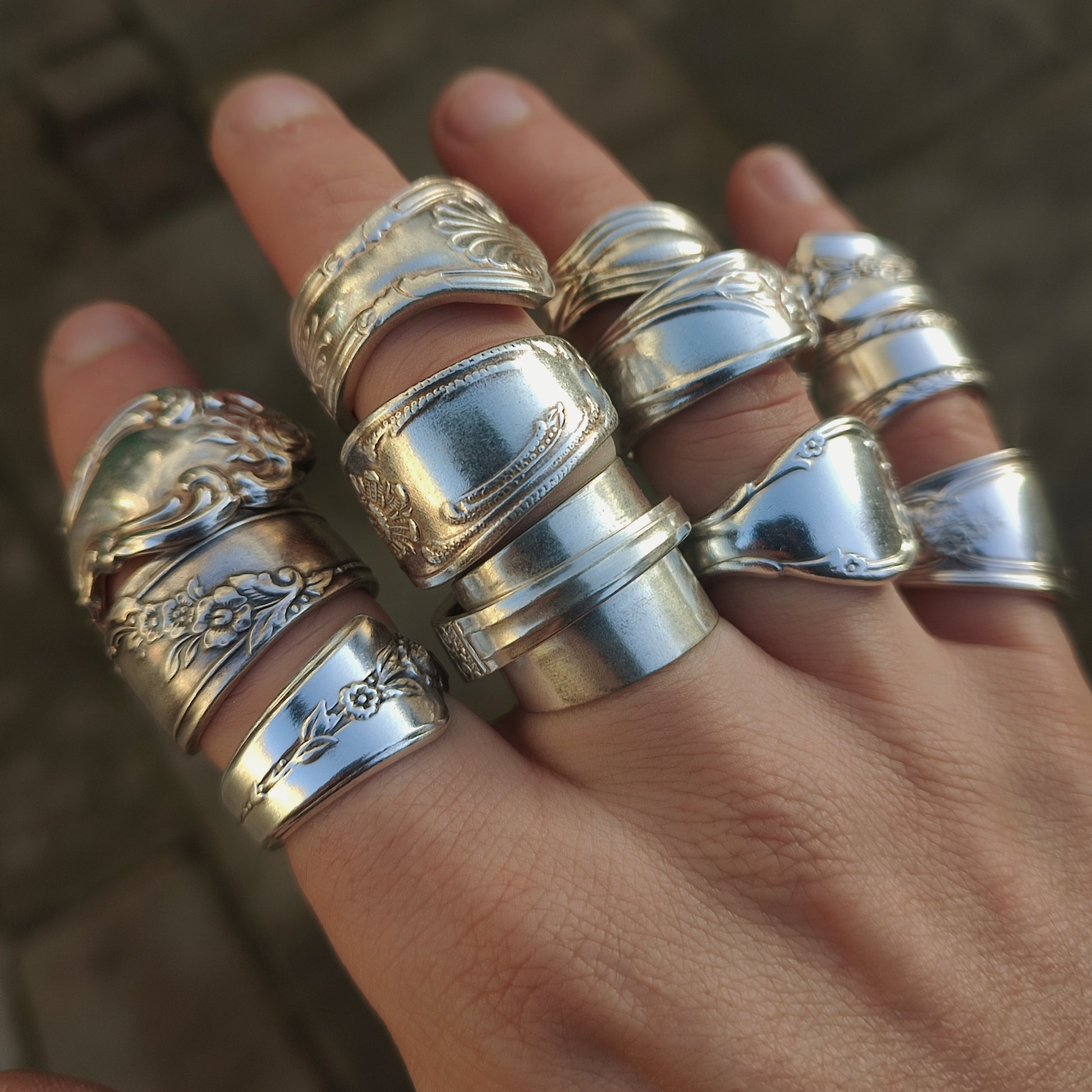 Hand wearing multiple spoon rings with intricate designs on a blurred background