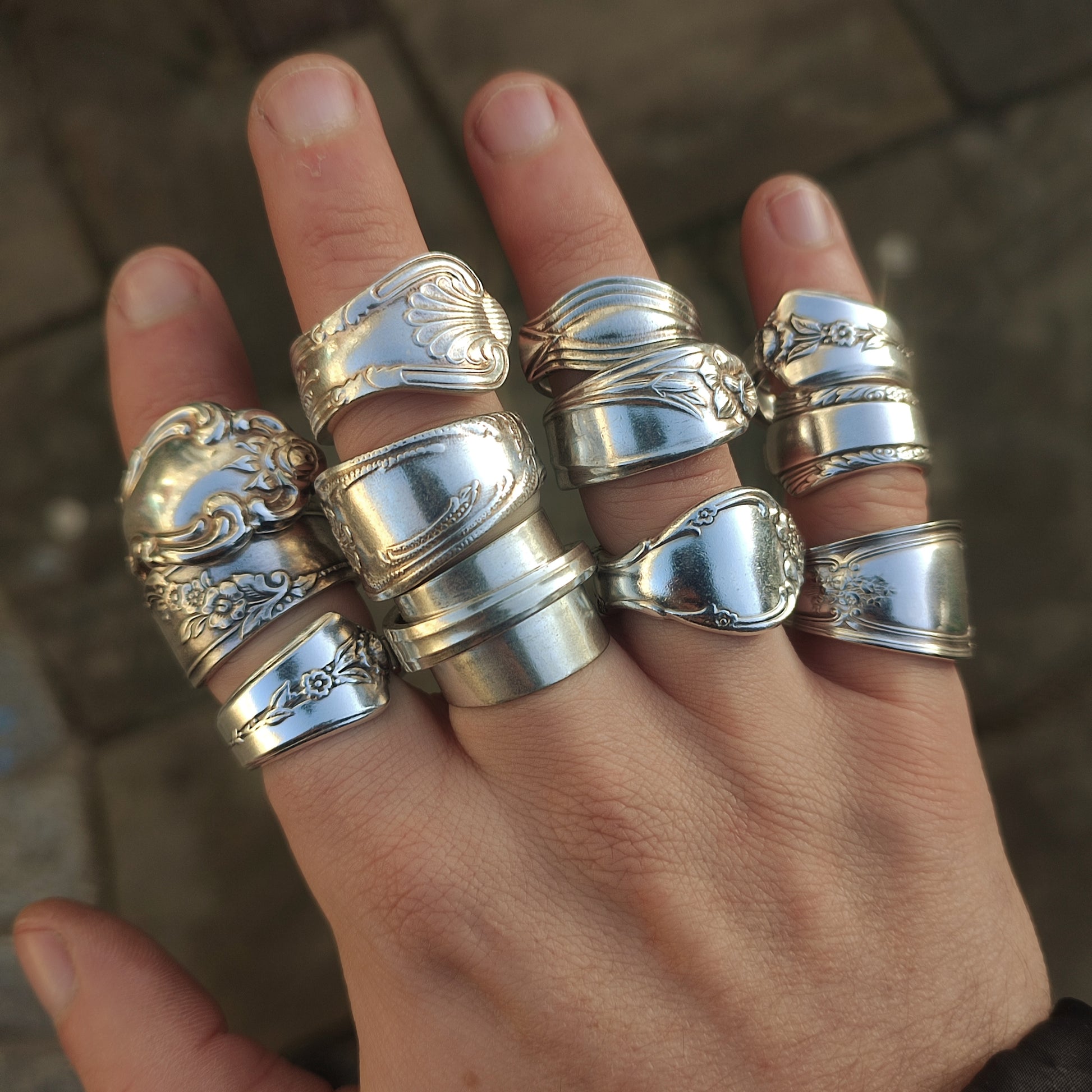 Hand wearing multiple silver spoon rings on a blurred background
