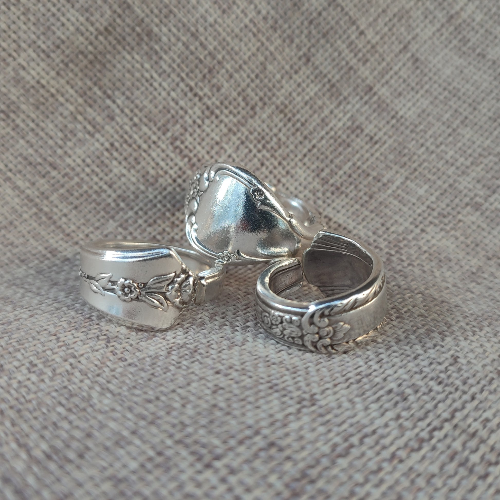 Three s rings with intricate designs on a textured linen fabric background