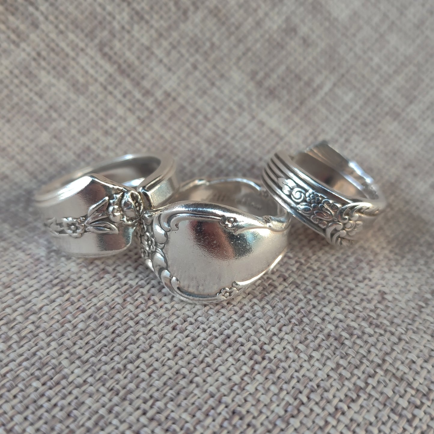 Three spoon rings with intricate designs on a textured fabric background