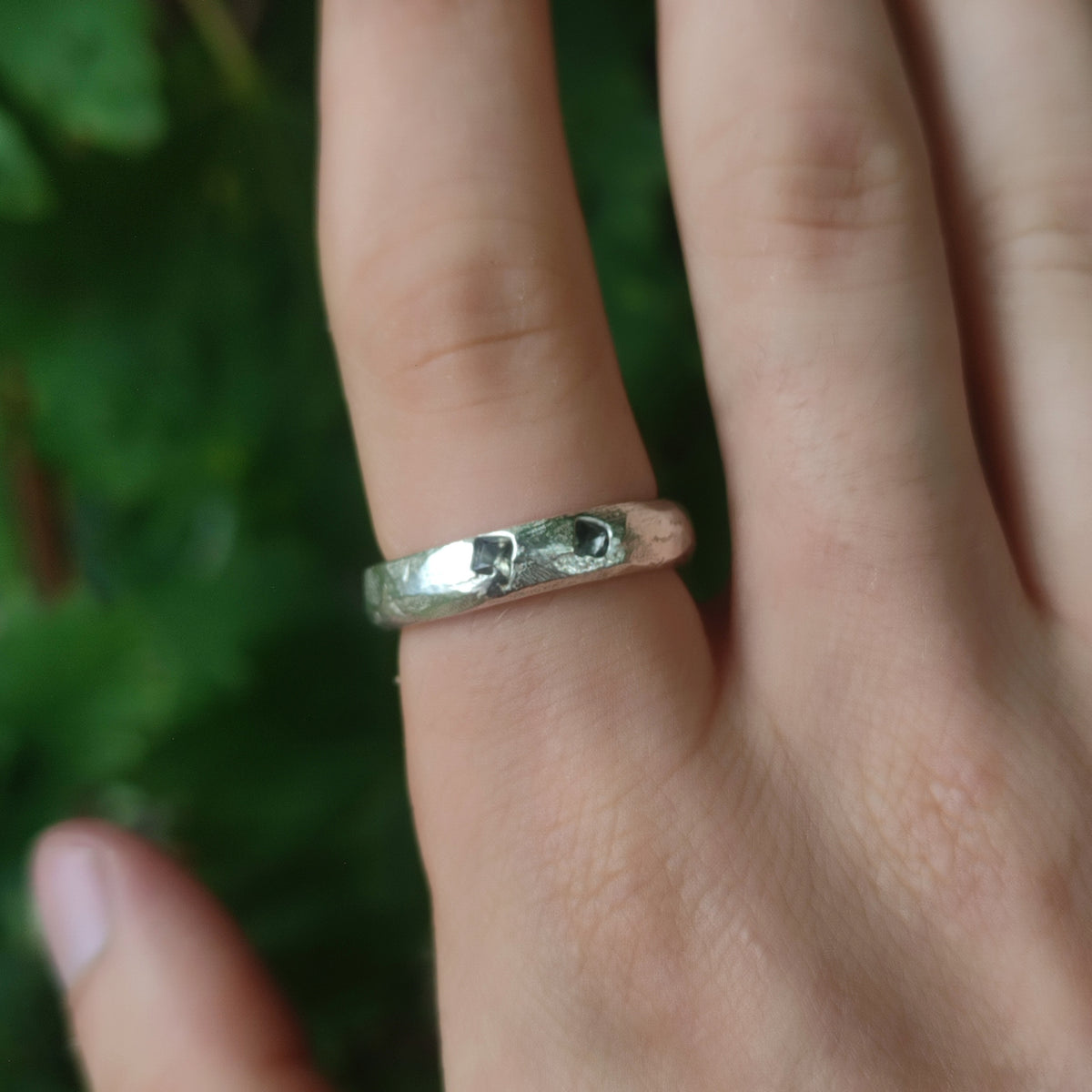 Silver teal sapphire ring worn on finger against a natural green background, showing sand cast texture"