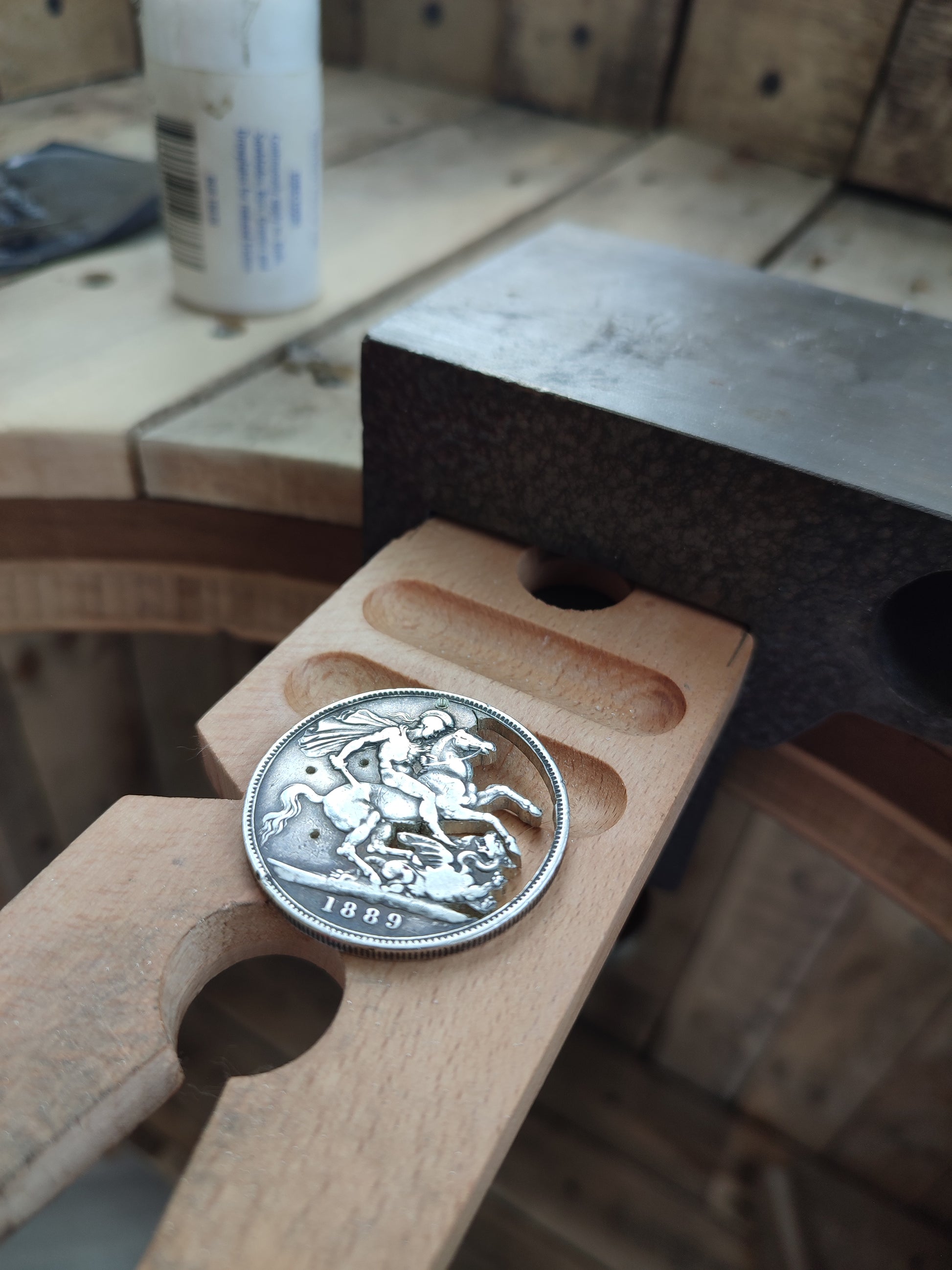 Silver coin with a soldier and horse design held in a wooden vise on a workshop bench.