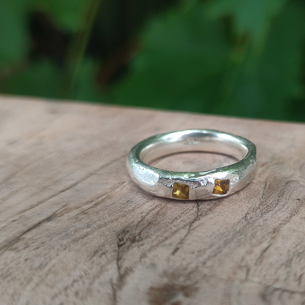 A sterling silver ring with two small yellow sapphires, viewed from a slightly elevated position, resting on a wooden surface 