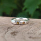 A  sterling silver ring with two square yellow sapphires, resting on a rustic wooden surface with a blurred green background.
