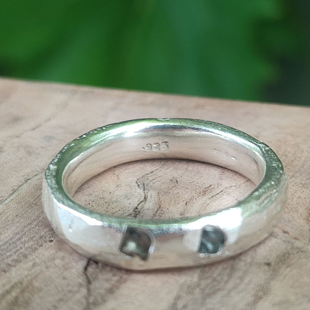 Inside of a sterling silver ring showing .925 hallmark, with teal sapphire stones visible on the band